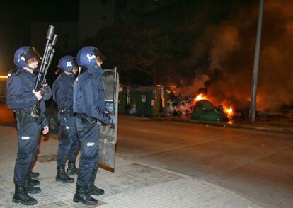 Agentes antidisturbios vigilan ante unos contenedores ardiendo.