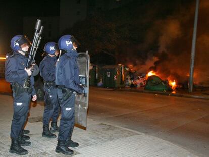 Agentes antidisturbios vigilan ante unos contenedores ardiendo.