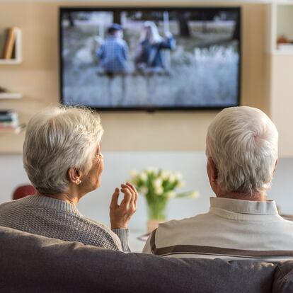 Senior couple sitting on sofa and watching television show at home.