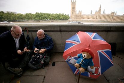 Dos hombres sentados junto a un peluche del oso Paddington mientras esperan para despedirse de la monarca en Londres, este miércoles.