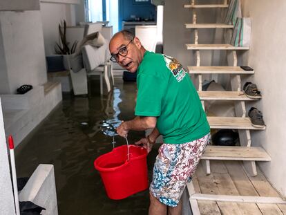 Armando, un vecino venezolano recién llegado al barrio del Cabanyal, con la casa inundada, achica agua con un cubo.