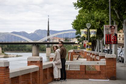 Una pareja observa el río Ebro en Tortosa, junto a carteles electorales con las imágenes de Salvador Illa o Pere Aragonès.