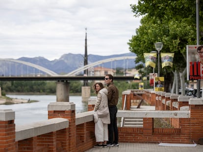 Una pareja observa el río Ebro en Tortosa, junto a carteles electorales con las imágenes de Salvador Illa o Pere Aragonès.