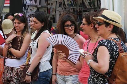 Asistentes a la feria combaten el calor con un abanico.