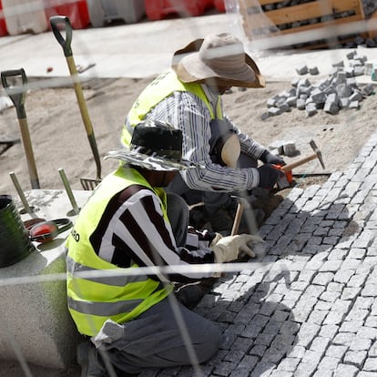 Dos obreros de la construcción pavimentan la acera en la calle Alcalá, este lunes en Madrid.