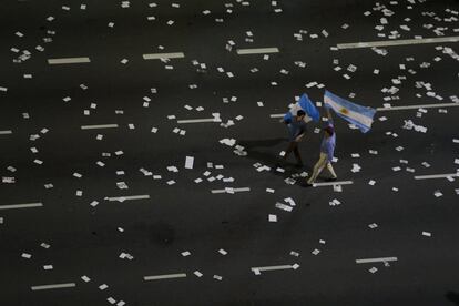 Dos seguidores del candidato argentino a la presidencia del Gobierno, Mauricio Macri, portan dos banderas por una calle llena de folletos en una calle en el centro de Buenos Aires.