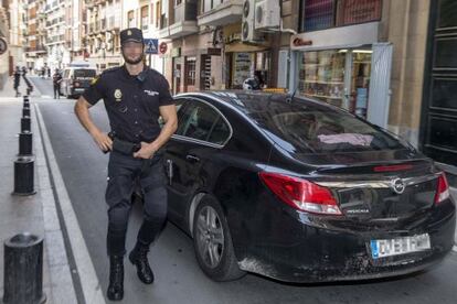 Un policia custodia un dels cotxes que traslladen els agents detinguts.