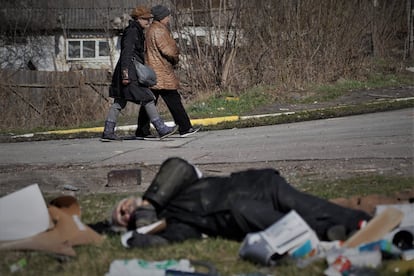 Luba, de 61 años (izquierda), y Luda, de 69, pasan por delante de un cadáver que lleva varios días delante de un supermercado atacado durante la guerra en Bucha. Algunas de estas personas pueden haber muerto en los bombardeos. Otras muchas presentan señales que sugieren que fueron ejecutadas.