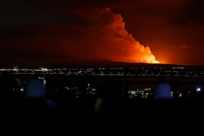 People watch as the night sky is illuminated caused by the eruption of a volcano on the Reykjanes peninsula of south-west Iceland seen from the capital city of Reykjavik, Monday Dec. 18, 2023.