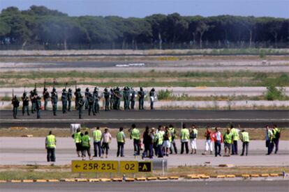 En primer término, los trabajadores de Iberia ocupan, el viernes pasado, las pistas de El Prat. Al fondo, agentes antidisturbios de la Guardia Civil.