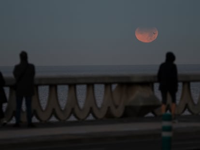 Tres personas observan el eclipse lunar parcial desde A Coruña, este viernes, en A Coruña, Galicia.