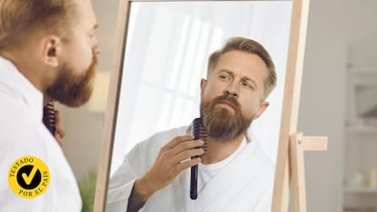 Un hombre peinándose la barba frente al espejo.