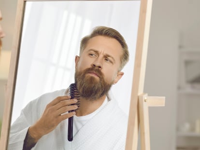 Un hombre peinándose la barba frente al espejo.