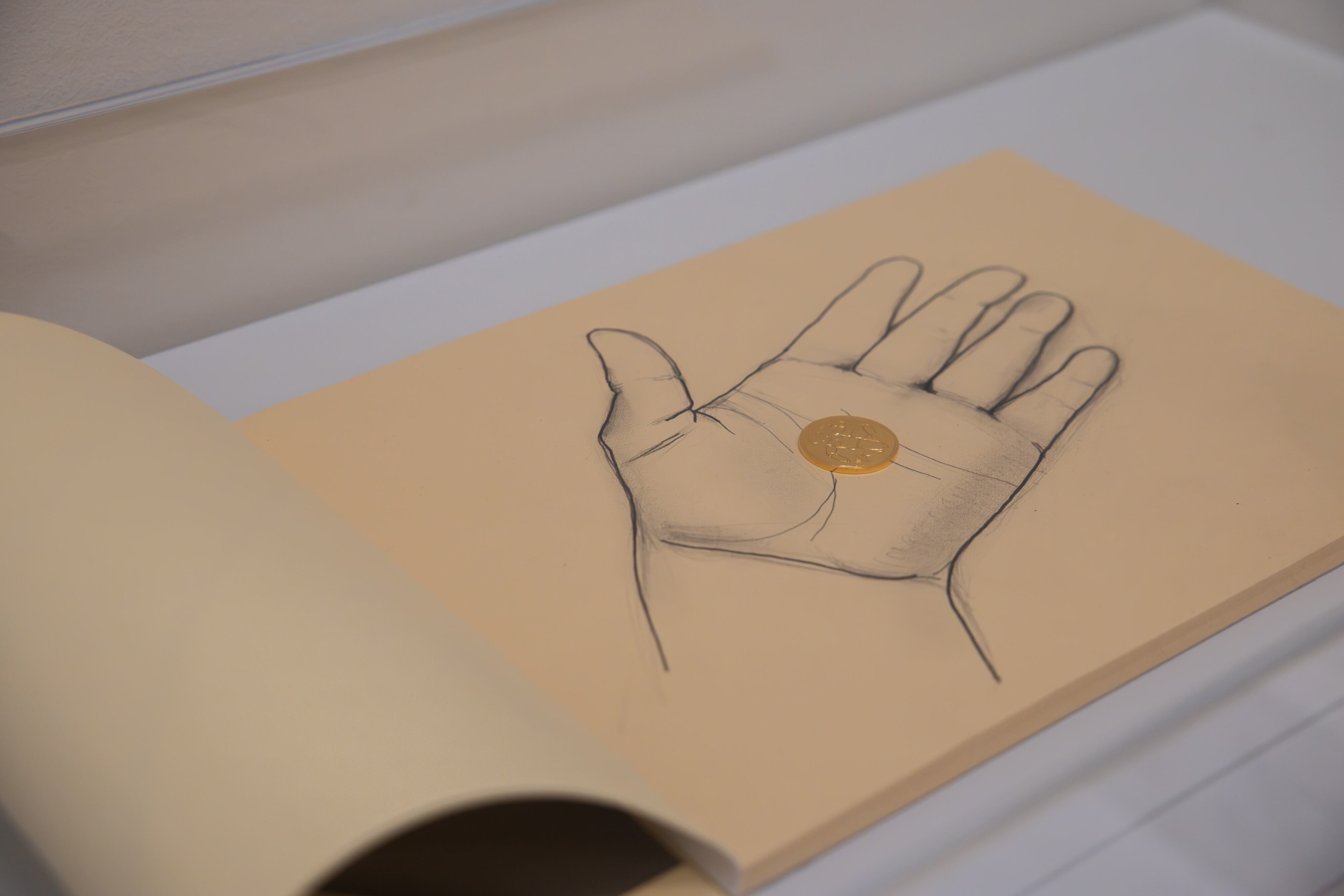 Imagen de la obra ‘Dismembered’ de Dora García, en la que se aprecia el bosquejo de una mano sosteniendo una moneda de plata chapada en oro.