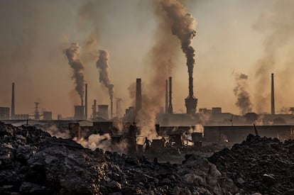 Smoke billows from a large steel plant as a Chinese labourer works at an unauthorized steel factory, foreground, on November 4, 2016 in Inner Mongolia, China