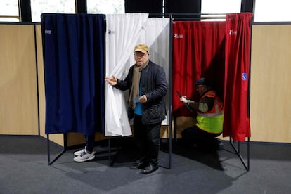 Un votante sostiene su papeleta, mientras un operario de mantenimiento trabaja en una cabina electoral en Le Touquet, en el norte de Francia, ciudad en la que ha votado el presidente, Emmanuel Macron.