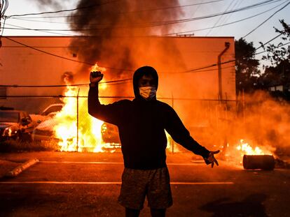 Manifestante ergue o punho diante de carros queimados, na quarta-feira, em Minneapólis.