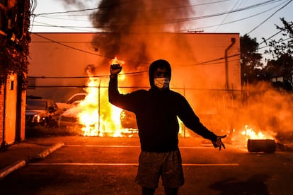 Manifestante ergue o punho diante de carros queimados, na quarta-feira, em Minneapólis.