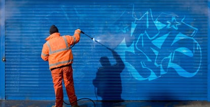 Un hombre tapa un grafiti en el cierre metálico de un comercio. 