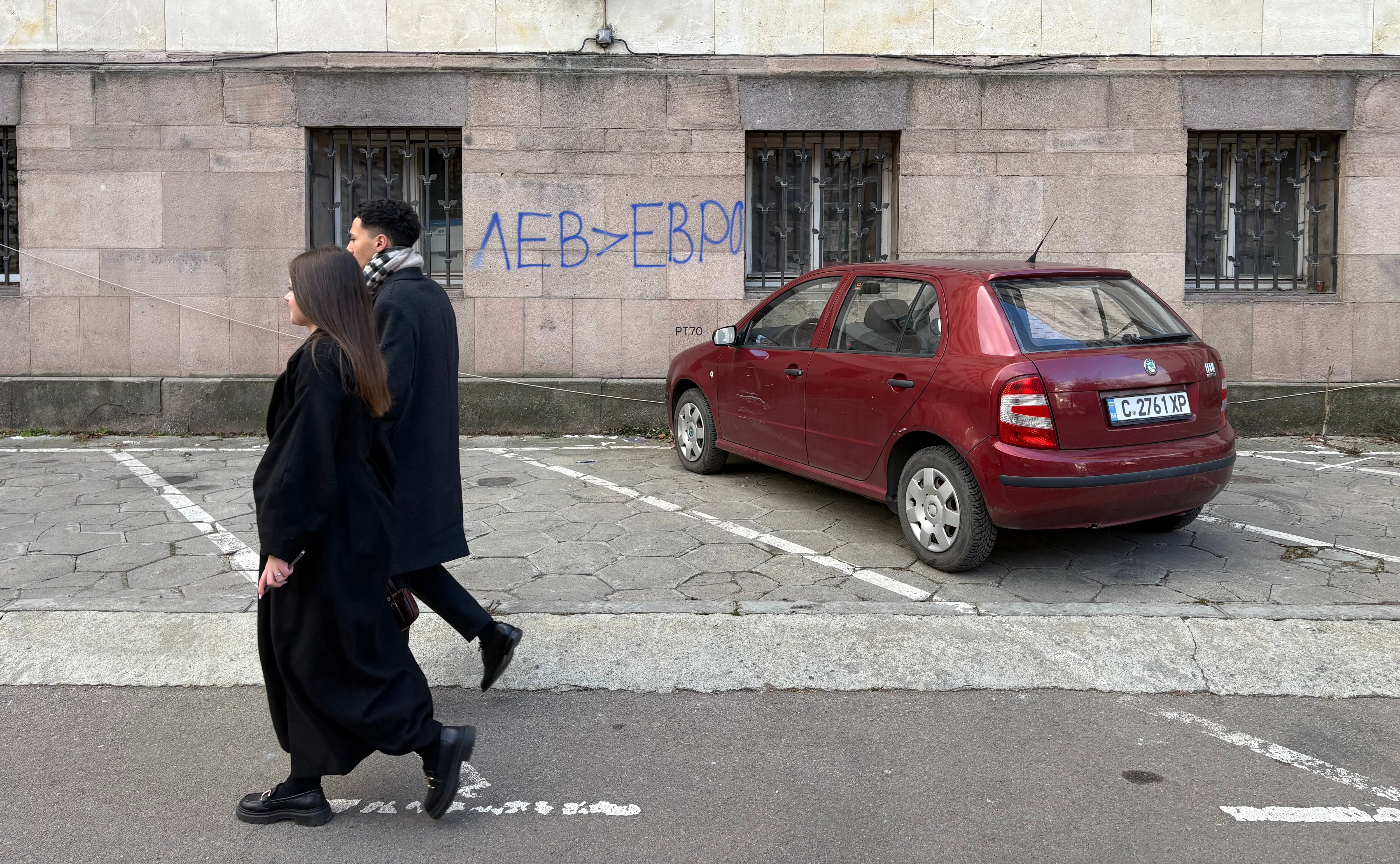 Dos jóvenes pasan delante de una pintada en la sede del Gobierno en la que se señala que se prefiere la leva al euro, el pasado viernes.