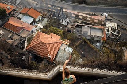 Uma mulher observa de sua sacada as casas queimadas em Campo da Barca, ilha da Madeira.