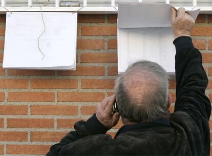 Una hombre consulta en un listado en qué mesa electoral debe votar en el colegio público Pablo Picasso de Madrid