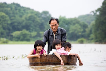 Un hombre empuja una cuba donde transporta a sus hijas para poder a casa después de la escuela, en una de las zonas inundadas de Duchang, provincia de Jiangxi, China, el miércoles 27 de julio. 