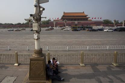 Un grupo de hombres lee a la sombra de unas cámaras de vigilancia en la plaza de Tiananmen.