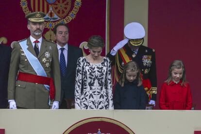 El Rey, la Reina y sus hijas saludan al paso de la bandera por la tribuna de honor.