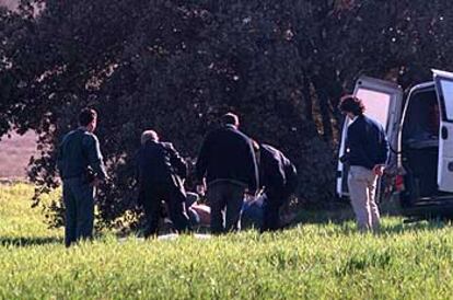 Empleados de la funeraria trasladan uno de los cadáveres encontrados en encinar de Villanueva de Perales