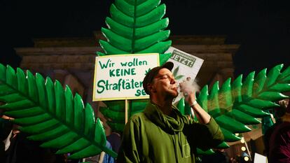 Un hombre fuma frente a un cartel que dice "No queremos ser criminales" en la Puerta de Brandeburgo, en Berlín, la noche del domingo al lunes.