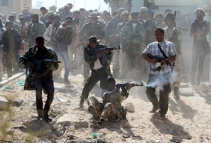 Combatientes del Consejo Nacional Transitorio Libio, disparan sobre posiciones de leales a Gadafi en una calle de Sirte; mientras, sus compañeros de armas en la siguiente línea ríen y toman fotografías del momento.