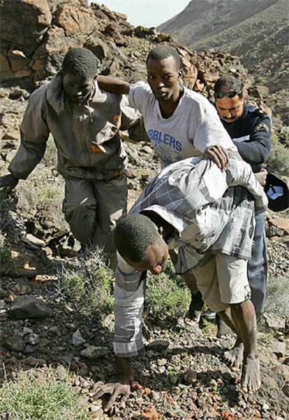 Un gendarme marroquí, que participaba en una patrulla conjunta, ayuda a tres subsaharianos a subir por los riscos.