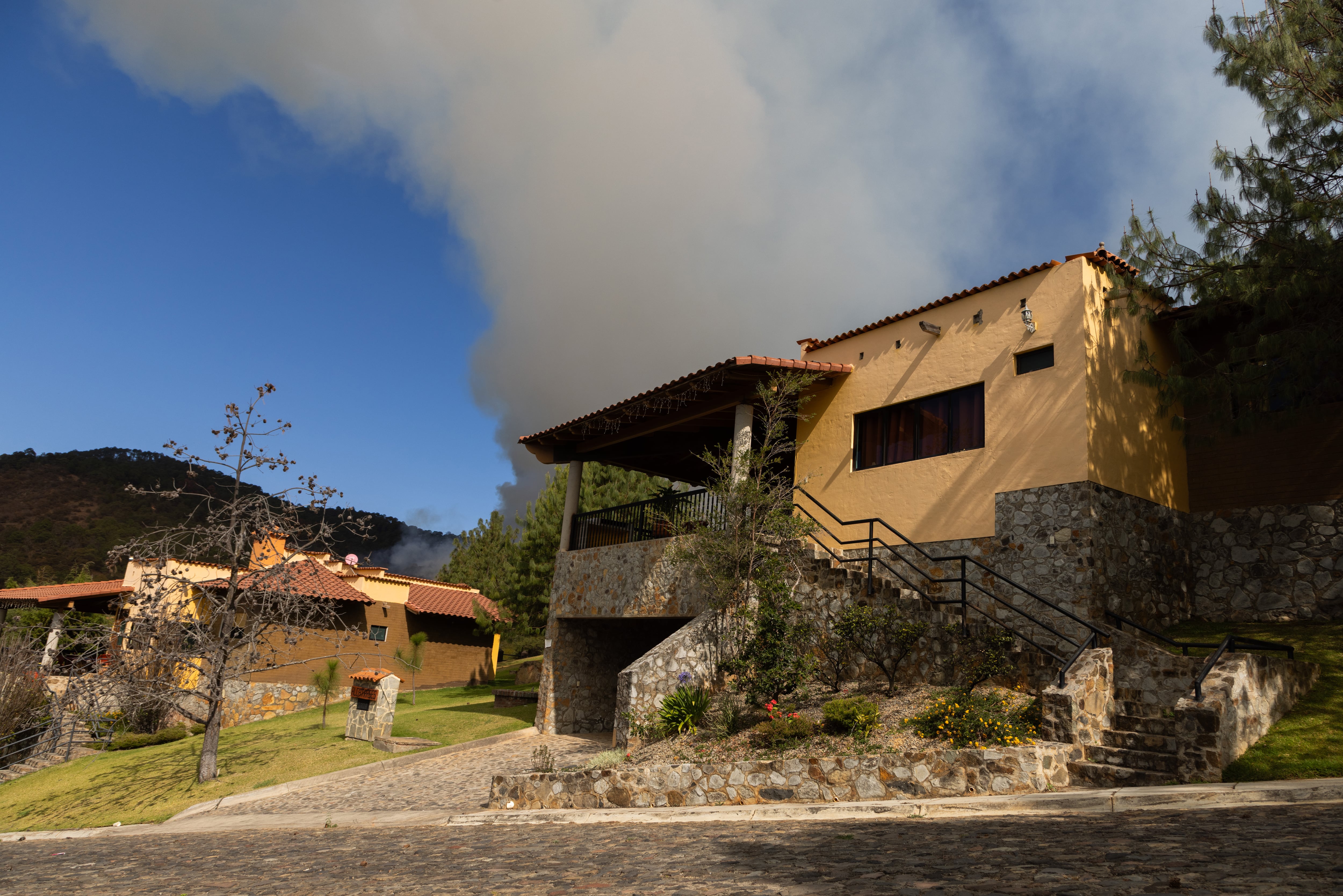 Fachada de una de las cabañas, detrás la nube del incendio que comenzó el 22 de febrero.