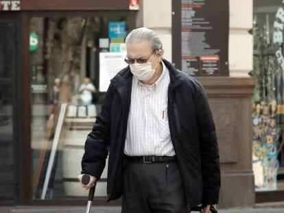 Una persona mayor protegida con mascarilla arrastra un carro frente a un comercio cerrado, en Valencia.