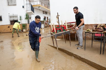 El párroco Carlos Samuel (izquierda) de la iglesia de la Encarnación de la localidad malagueña de Benamargosa limpia de barro los pequeños pasos con imágenes de un cristo y una virgen tras las fuertes lluvias caídas este miércoles.