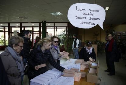 Los votantes seleccionan sus papeletas en una mesa de votación con un cartel colgando sobre la mesa de un colegio de Madrid.