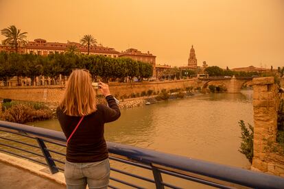 Una mujer hace una fotografía con su móvil del aspecto que presentaba la ciudad de Murcia esta tarde, con un alto número de partículas y polvo en suspensión.
