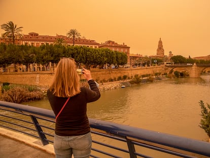 Una mujer hace una fotografía con su móvil del aspecto que presentaba la ciudad de Murcia esta tarde, con un alto número de partículas y polvo en suspensión.