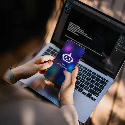 Businesswoman using chatting AI chatbot virtual assistance app on smartphone to assist her while working on laptop in office park. Using AI technology at work. Online robot system. Concept of VR and AR technologies. People, AI, innovation and technology