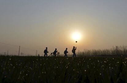 Unos estudiantes juegan con sus pelotas de fútbol mientras caminan por campos de cultivo para llegar a la escuela en Sunji (China).