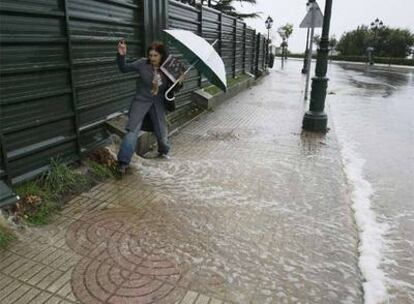 Una mujer intenta cruzar una acera en Vigo, inundada a consecuencia de las fuertes lluvias.
