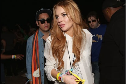 Lindsay Lohan con un look blanco compuesto por camisa y top de encaje y gafas de sol amarillas.