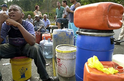 Un joven, rodeado de bidones de gasolina, espera junto a un surtidor de gasolina en Caracas.