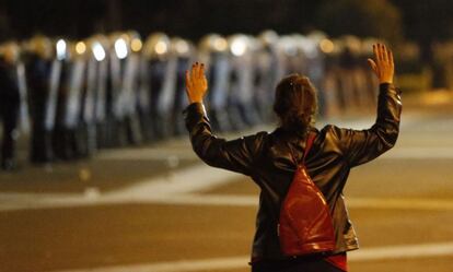 Una mujer levanta las manos frente a una hilera de policías antidisturbios.