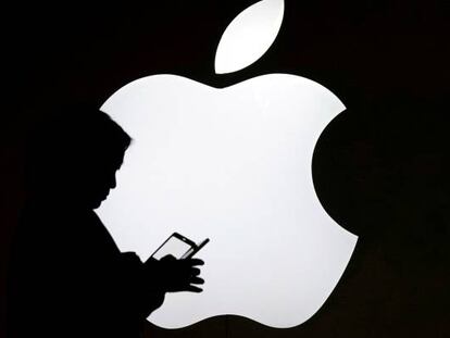 Una persona consulta un móvil delante de un logotipo de Apple, en Shangai.