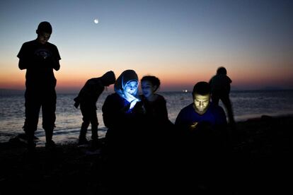 Refugiados checam o celular após descer de um bote inflável na ilha grega de Kos, depois de cruzar o mar Egeu.