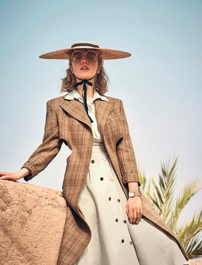 Abrigo entallado de Céline, camisa de organza de Blumarine, falda abotonada de Loewe, sombrero de paja de Jacquemus y gafas hexagonales de Kaleos. En la mano izquierda, anillos de Oui Petit y reloj con correa de piel de Fossil. El colorete Cushion Blush Subtil Spring (43 euros), de Lancôme, en tono 02 Rose Lemonade, potencia el efecto buena cara.