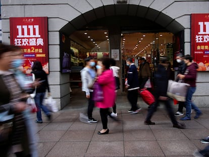 Varias personas pasan por delante de un comercio con carteles del Día del Soltero, este jueves en Shanghái (China).