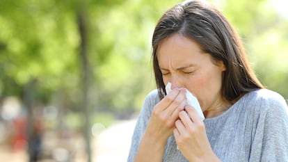 Una mujer estornuda en un parque a causa del polen.